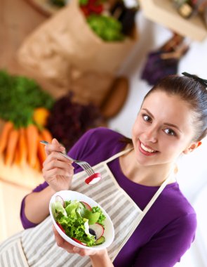 Genç kadın modern mutfakta taze salata yiyor.