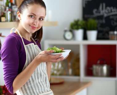 Genç kadın modern mutfakta taze salata yiyor.