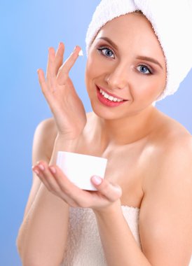 Güzel genç kadın yüzünde gri arka plan üzerinde izole bir krem uygulamak