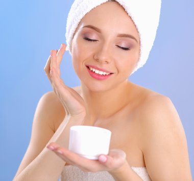 Güzel genç kadın yüzünde gri arka plan üzerinde izole bir krem uygulamak