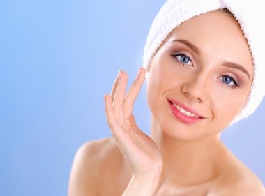 Güzel genç kadın yüzünde gri arka plan üzerinde izole bir krem uygulamak