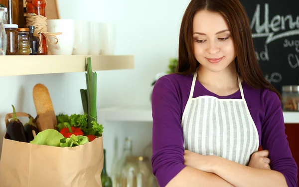 Young woman standing in her kitchen near desk with shopping bags — Stock Photo, Image