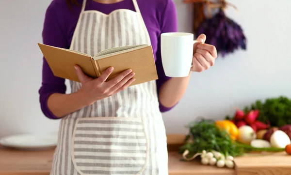 Jonge vrouw die kookboek leest in de keuken, op zoek naar recept — Stockfoto