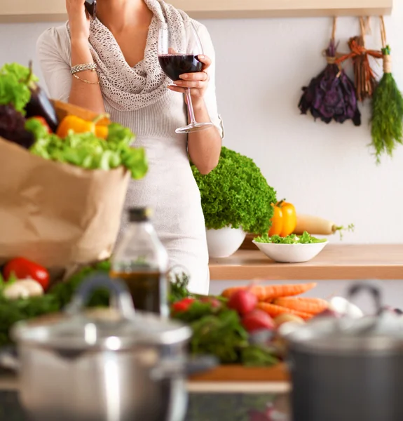 Mujer joven cortando verduras en la cocina, sosteniendo una copa de vino —  Fotos de Stock