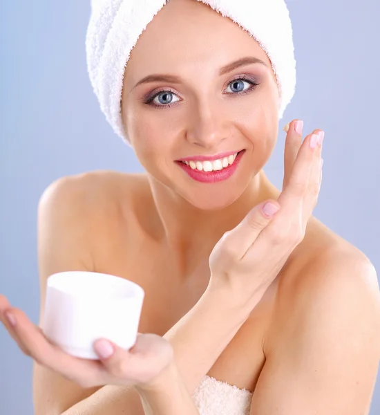 Mooie jonge vrouw, een crème op haar gezicht geïsoleerd op grijze achtergrond toe te passen — Stockfoto