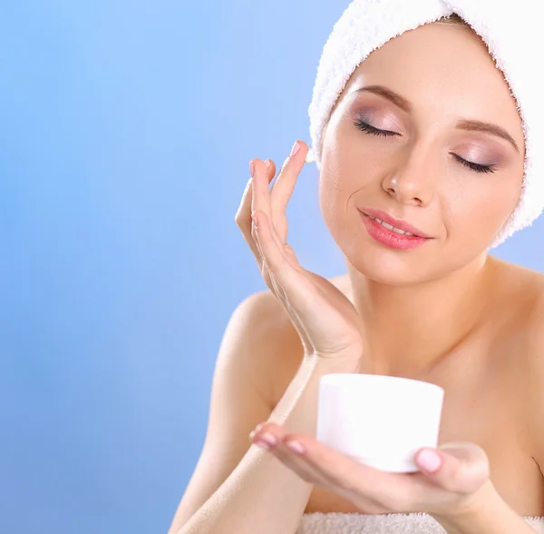 Hermosa joven aplicando una crema en su cara aislada sobre fondo gris —  Fotos de Stock