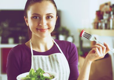Genç kadın modern mutfakta taze salata yiyor.