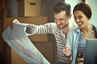 Genç bir çift yerde oturuyor ve yeni evin planına bakıyor.