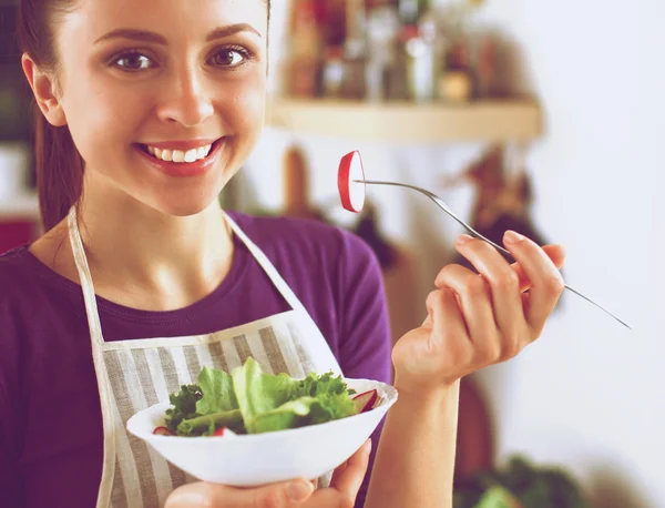 Mujer joven comiendo ensalada fresca en la cocina moderna — Foto de Stock