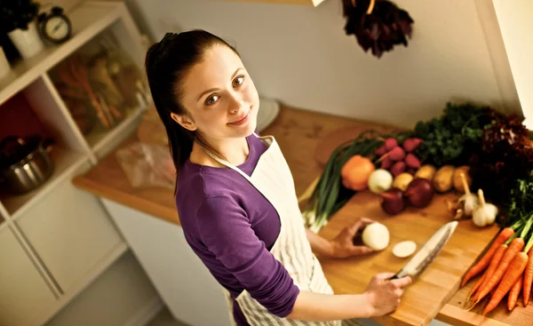 Jovem mulher cortando legumes na cozinha — Fotografia de Stock