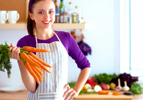 Счастливая молодая женщина с кучей моркови на кухне — стоковое фото