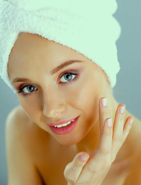 Hermosa joven aplicando una crema en su cara aislada sobre fondo gris —  Fotos de Stock