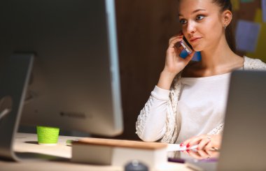 Ofiste çalışan genç kadın masada oturan ve telefonda konuşmak