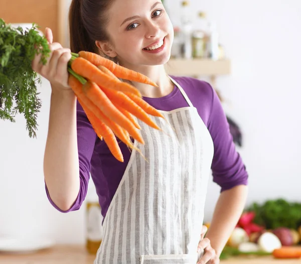 Happy young woman holding bunch of carrots in kitchen — Stock Photo, Image