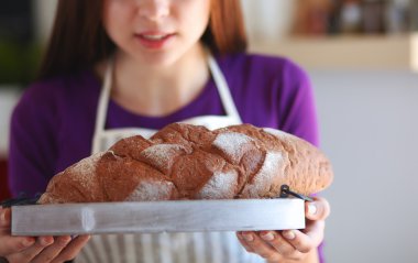 Genç bir kadın mutfağında lezzetli taze ekmek tutuyor.