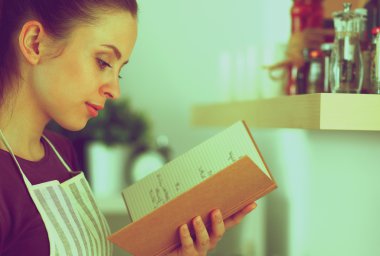 Mutfakta yemek kitabı okuyan genç bir kadın yemek tarifi arıyor.