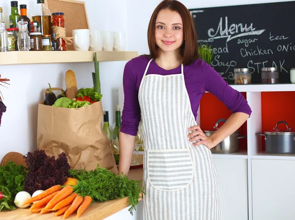 Young woman standing in her kitchen near desk with shopping bags — Stock Photo, Image