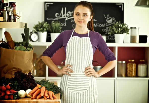 Jovem mulher de pé em sua cozinha perto da mesa com sacos de compras — Fotografia de Stock