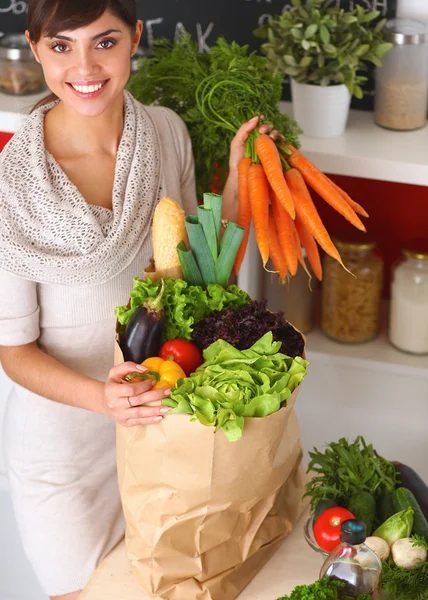 Gelukkig jong vrouw houden bos van wortelen in keuken — Stockfoto