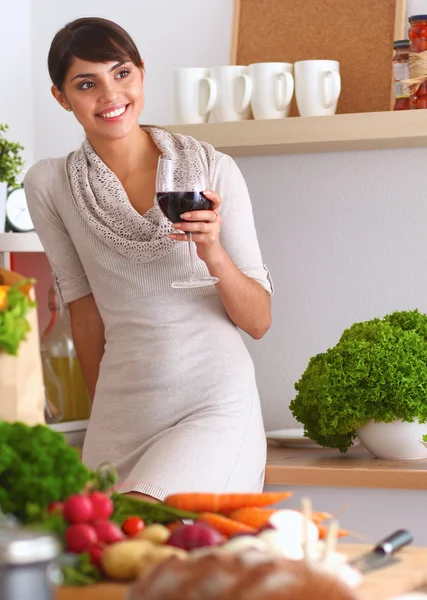 Mujer joven cortando verduras en la cocina, sosteniendo una copa de vino —  Fotos de Stock