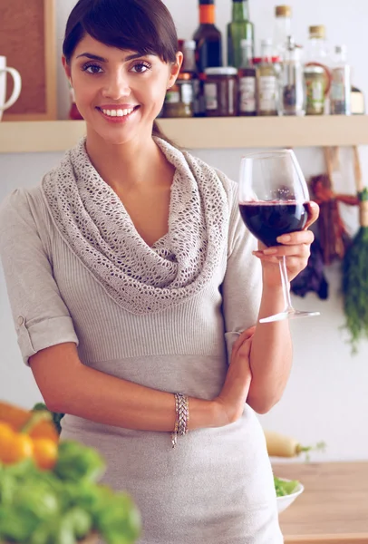 Jeune femme coupant des légumes dans la cuisine, tenant un verre de vin — Photo