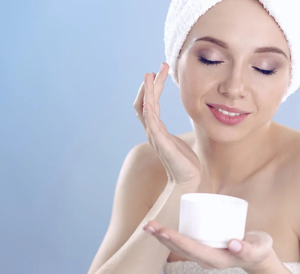 Bella giovane donna che applica una crema sul suo viso isolato su sfondo grigio — Foto Stock