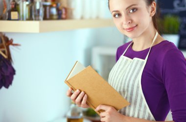 Mutfakta yemek kitabı okuyan genç bir kadın yemek tarifi arıyor.