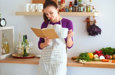 Mutfakta yemek kitabı okuyan genç bir kadın yemek tarifi arıyor.