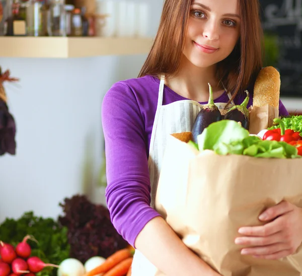 Jonge vrouw met boodschappentas met groenten Staande in de keuken — Stockfoto