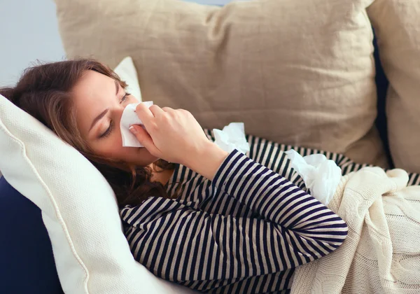 Retrato de una mujer enferma sonándose la nariz mientras está sentada en el sofá —  Fotos de Stock
