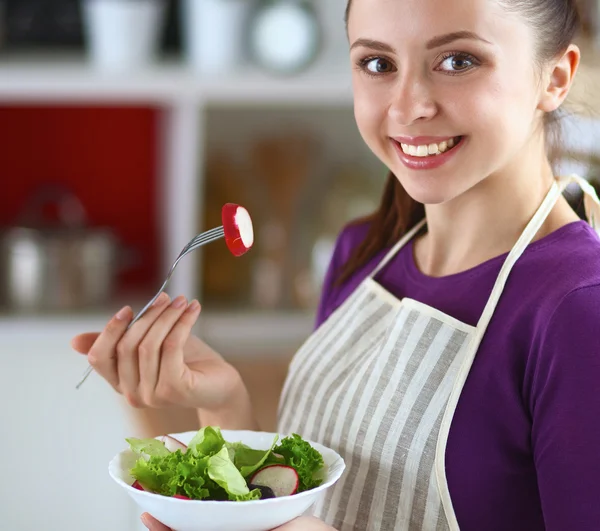 Une jeune femme mange de la salade dans sa cuisine . — Photo