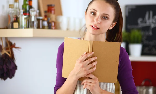 Mujer joven leyendo libro de cocina en la cocina, buscando receta —  Fotos de Stock