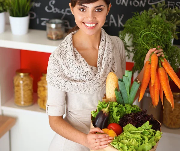 Una joven mujer de pie en su cocina sosteniendo una bolsa de comestibles. — Foto de Stock