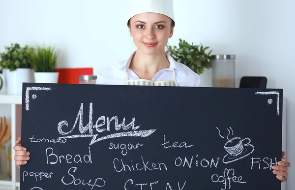 Женщина-повар держит доску с меню, стоит на кухне — стоковое фото