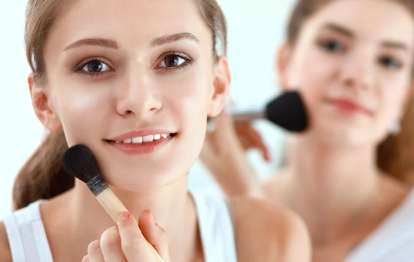Meninas bonitas olhando no espelho e aplicando cosméticos com uma escova grande — Fotografia de Stock