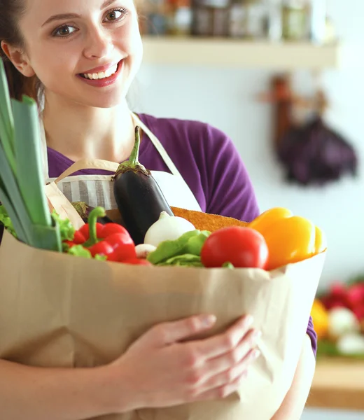 Jonge vrouw met boodschappentas met groenten Staande in de keuken — Stockfoto