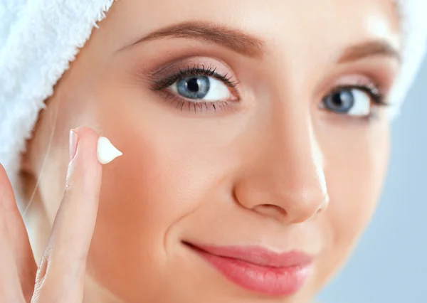 Beautiful young woman applying a creme on her face isolated on gray background — Stock Photo, Image