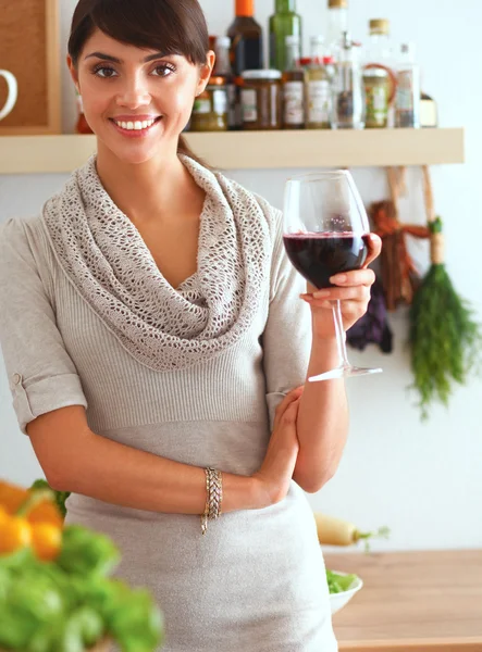 Junge Frau schneidet Gemüse in Küche und hält ein Glas Wein in der Hand — Stockfoto