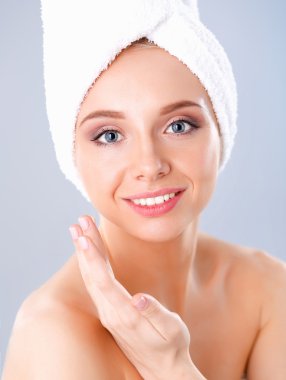 Güzel genç kadın yüzünde gri arka plan üzerinde izole bir krem uygulamak