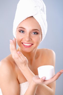 Güzel genç kadın yüzünde gri arka plan üzerinde izole bir krem uygulamak