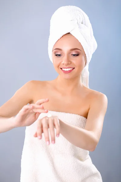 Schöne junge Frau Anwendung einer Creme auf ihr Gesicht isoliert auf grauem Hintergrund — Stockfoto