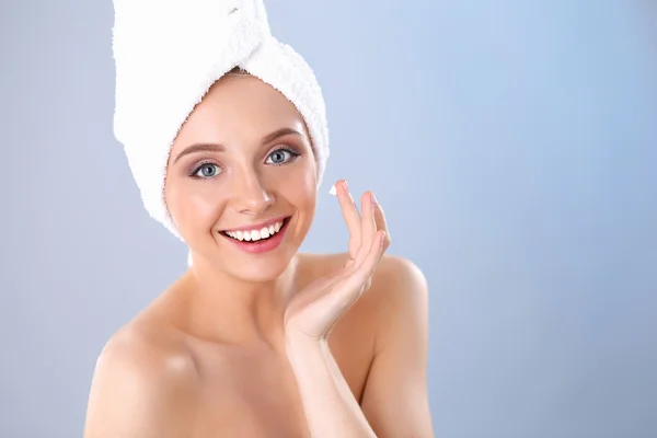 Schöne junge Frau Anwendung einer Creme auf ihr Gesicht isoliert auf grauem Hintergrund — Stockfoto