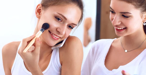Vackra flickor tittar i spegeln och tillämpa kosmetika med en stor borste — Stockfoto