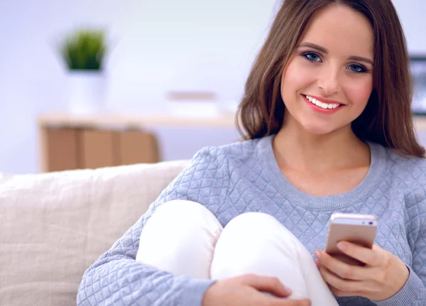 可愛いです女の子使用彼女のスマートフォン上のソファに自宅でザリビングルーム — ストック写真