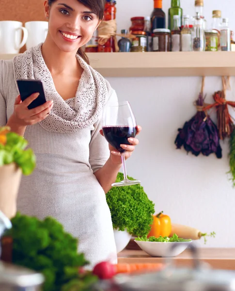 Young woman cutting vegetables in kitchen, holding a glass of wine — Stock Photo, Image