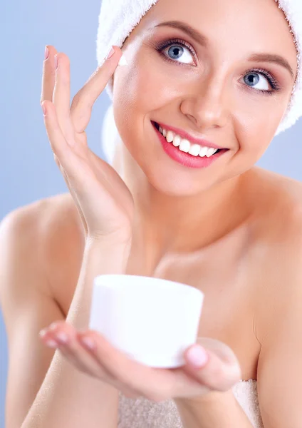 Mulher bonita aplicando um creme em seu rosto isolado em fundo cinza — Fotografia de Stock