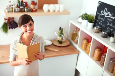 Mutfakta yemek kitabı okuyan genç bir kadın yemek tarifi arıyor.