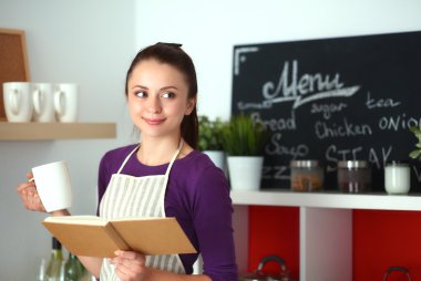 Mutfakta yemek kitabı okuyan genç bir kadın yemek tarifi arıyor.