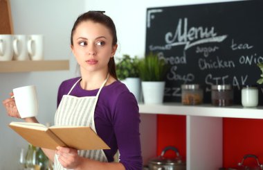 Mutfakta yemek kitabı okuyan genç bir kadın yemek tarifi arıyor.