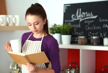 Mutfakta yemek kitabı okuyan genç bir kadın yemek tarifi arıyor.